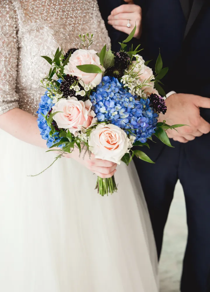 Couples holding embraced arms with a blue and pink bouquet